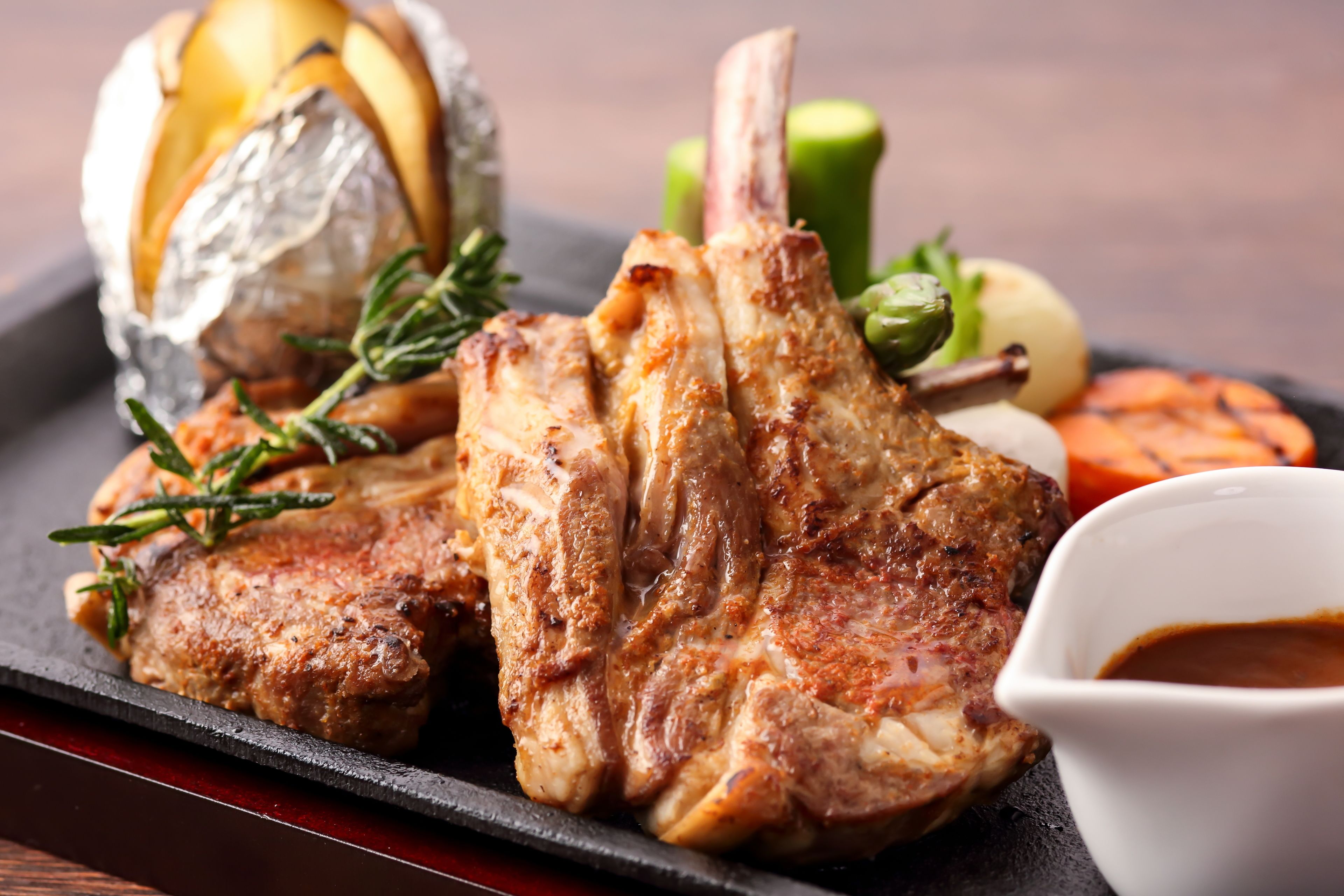 Un plato con carne a la parrilla, verduras y un recipiente pequeño con salsa.