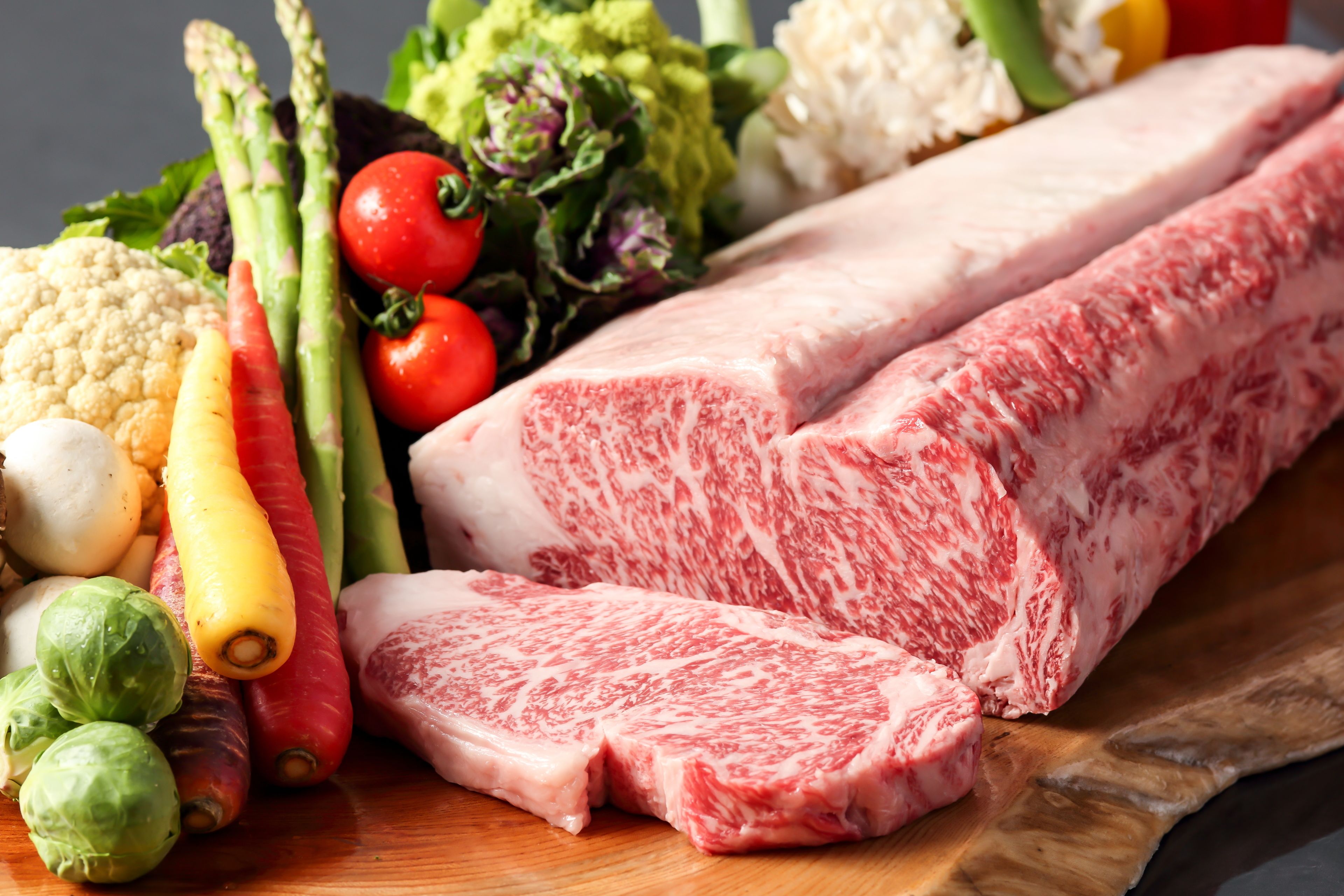 Une variété de légumes frais et un gros morceau de viande, le tout disposé sur une planche à découper en bois.