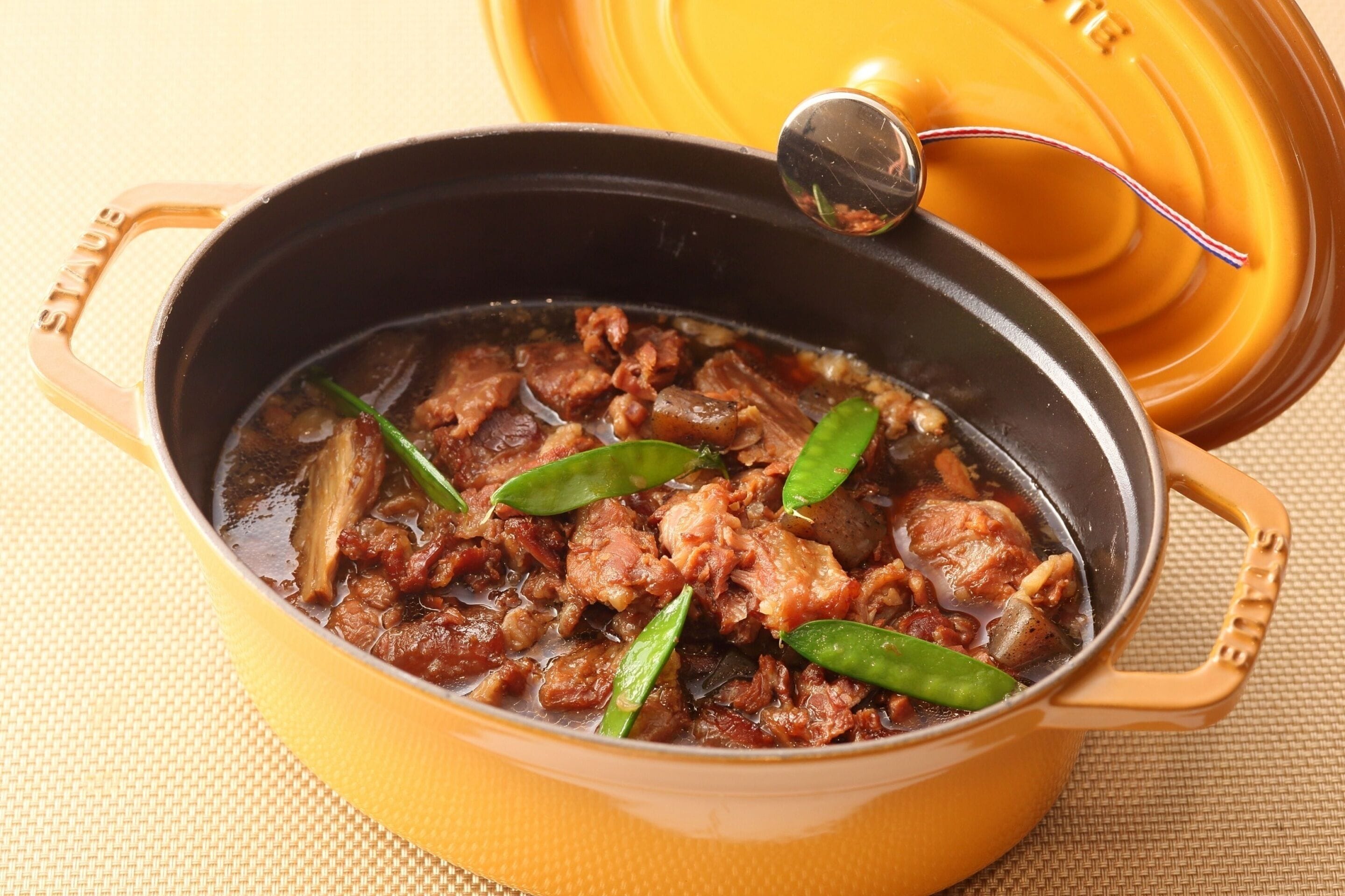 A pot of stew with meat and green beans on a yellow surface.