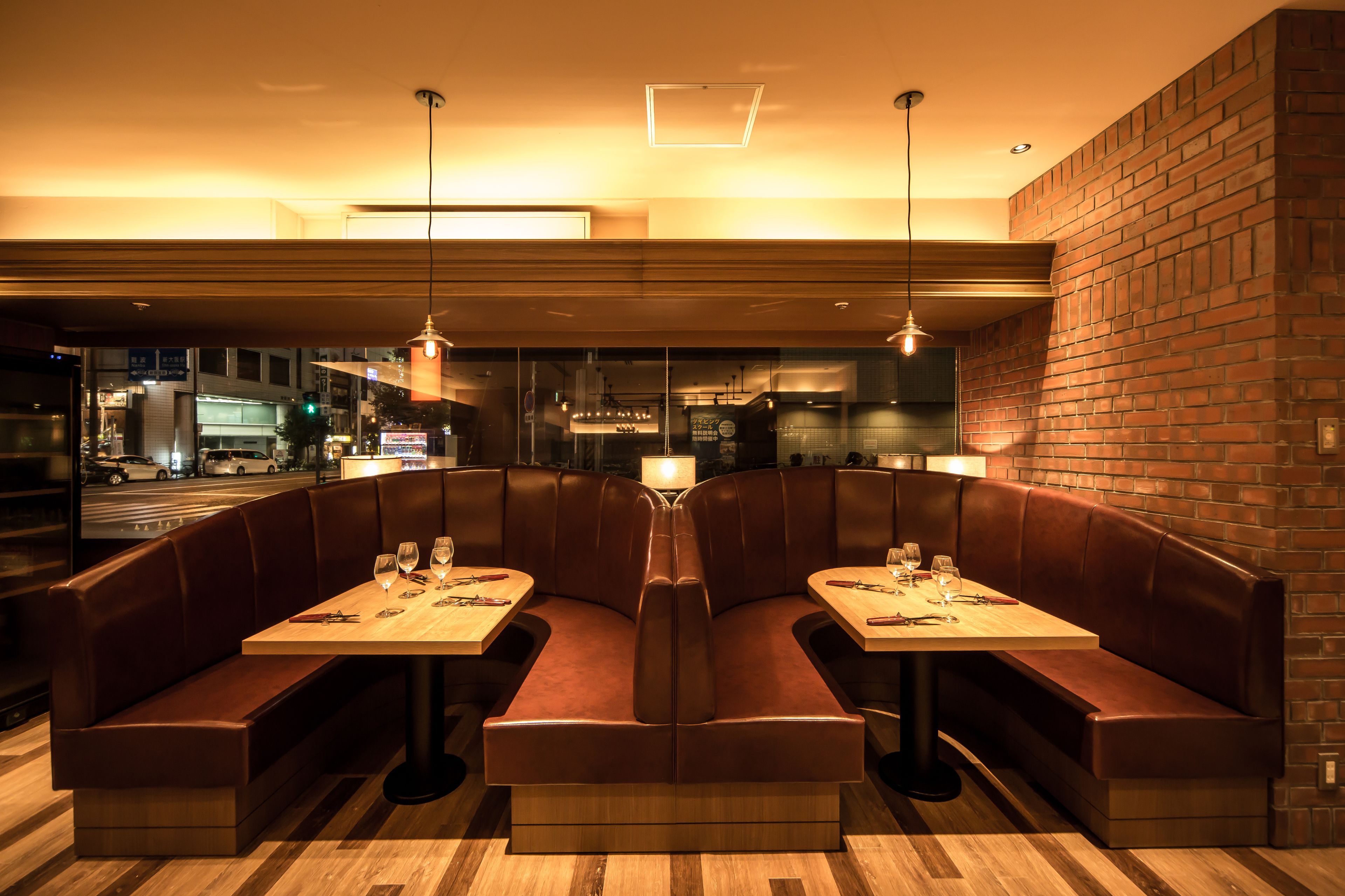 A restaurant with a booth seating arrangement, a wooden table, and pendant lighting.
