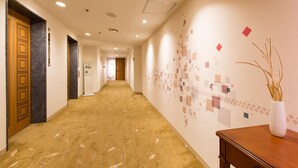 Un couloir d’hôtel doté d’un sol recouvert de moquette, de portes en bois et d’un mur orné d’un motif géométrique.