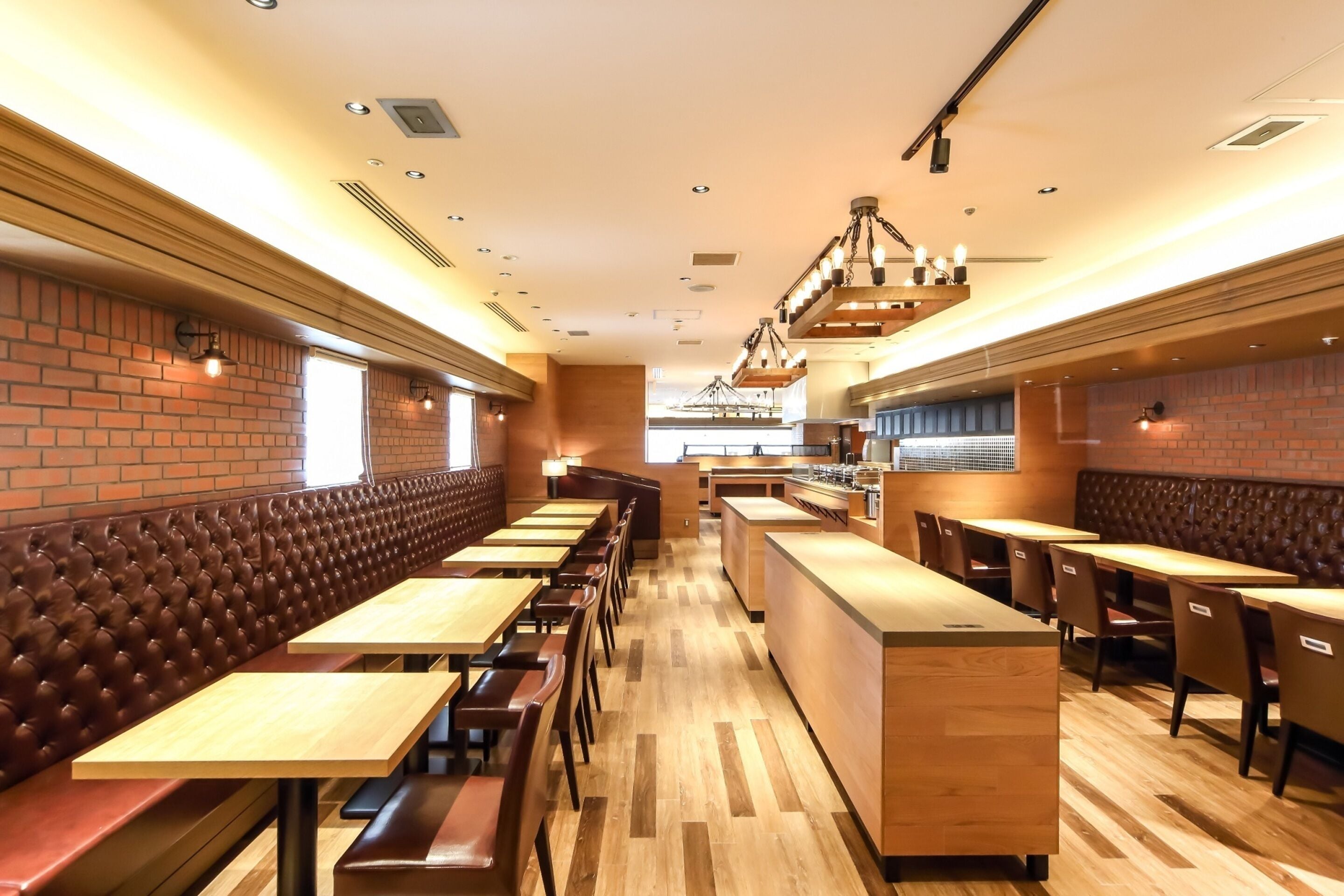 Een restaurant met lange houten tafels en comfortabele zitbanken, bakstenen muren en hanglampen.