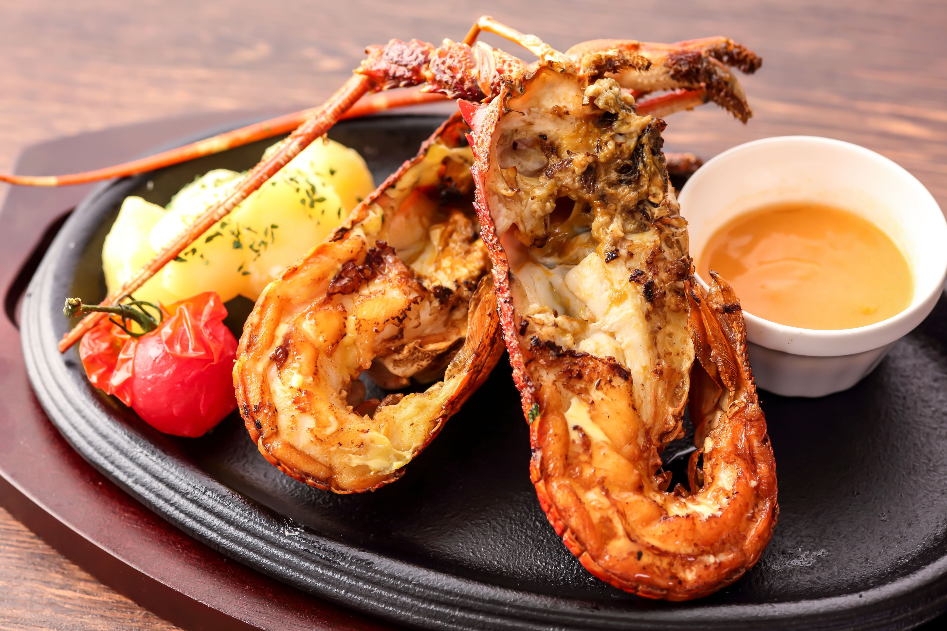 A lobster tail with a side of potatoes and a small bowl of sauce.