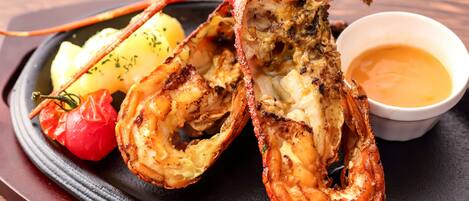A lobster tail with a side of potatoes and a small bowl of sauce.