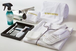 A set of toiletries including a spray bottle, a hairdryer, and a travel-sized hairbrush, along with neatly folded towels and a bathrobe with embroidered text.
