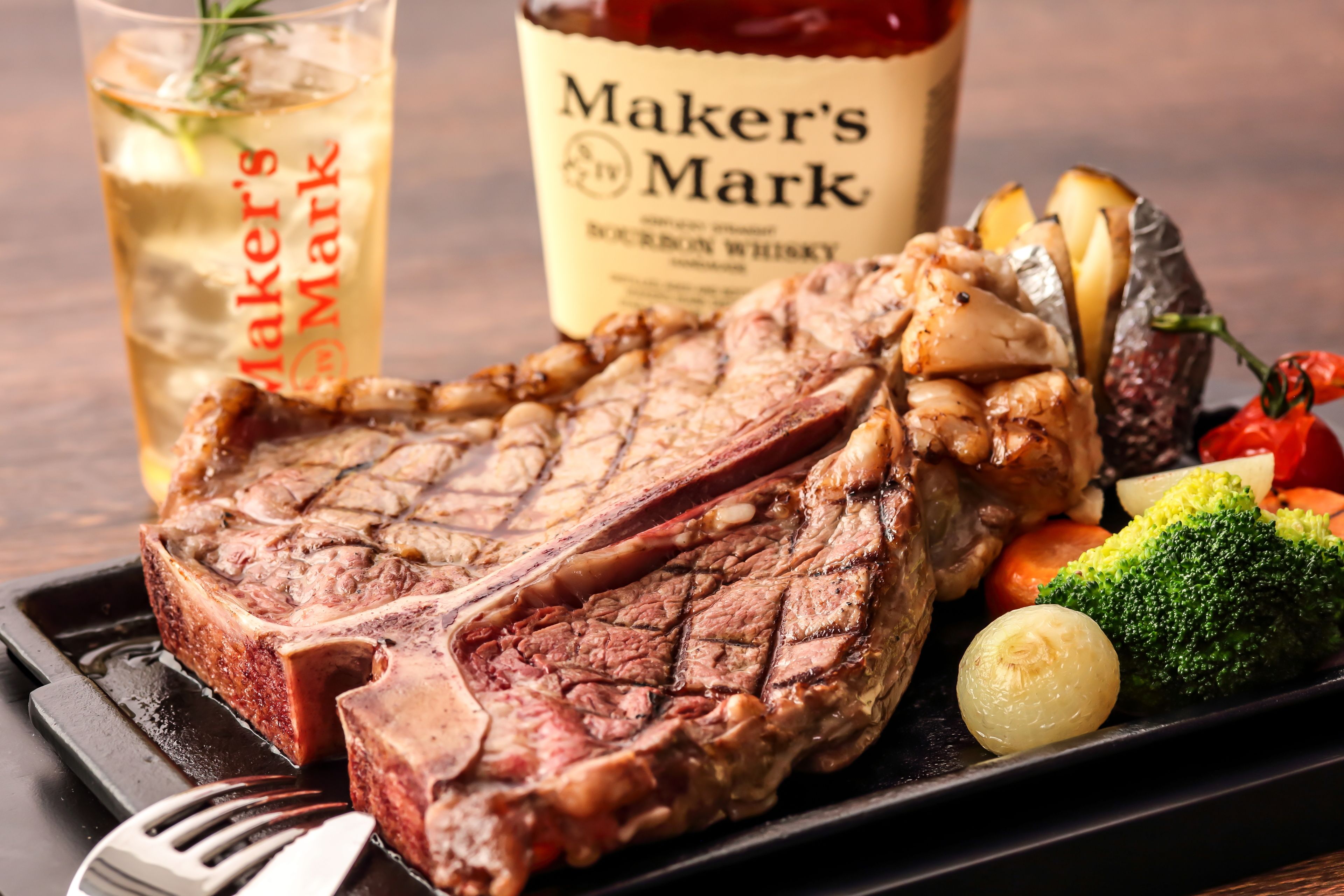 Un plato de carne con verduras y una botella de whisky bourbon Maker's Mark.