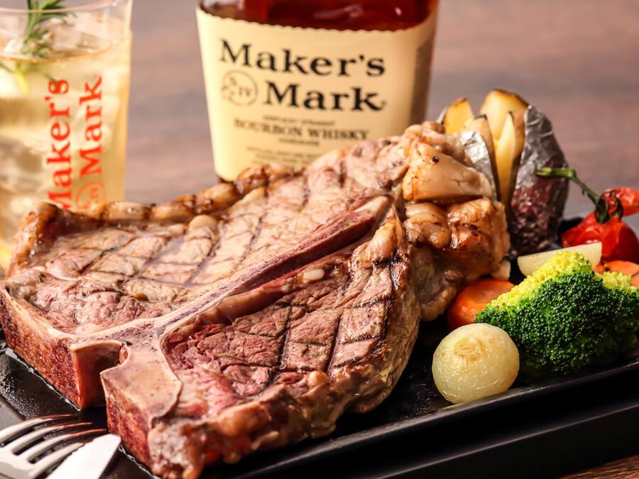 Un plato de carne con verduras y una botella de whisky bourbon Maker's Mark.
