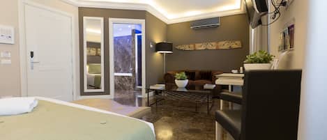 Habitación de hotel con cama, escritorio, silla, sofá, televisor y planta.