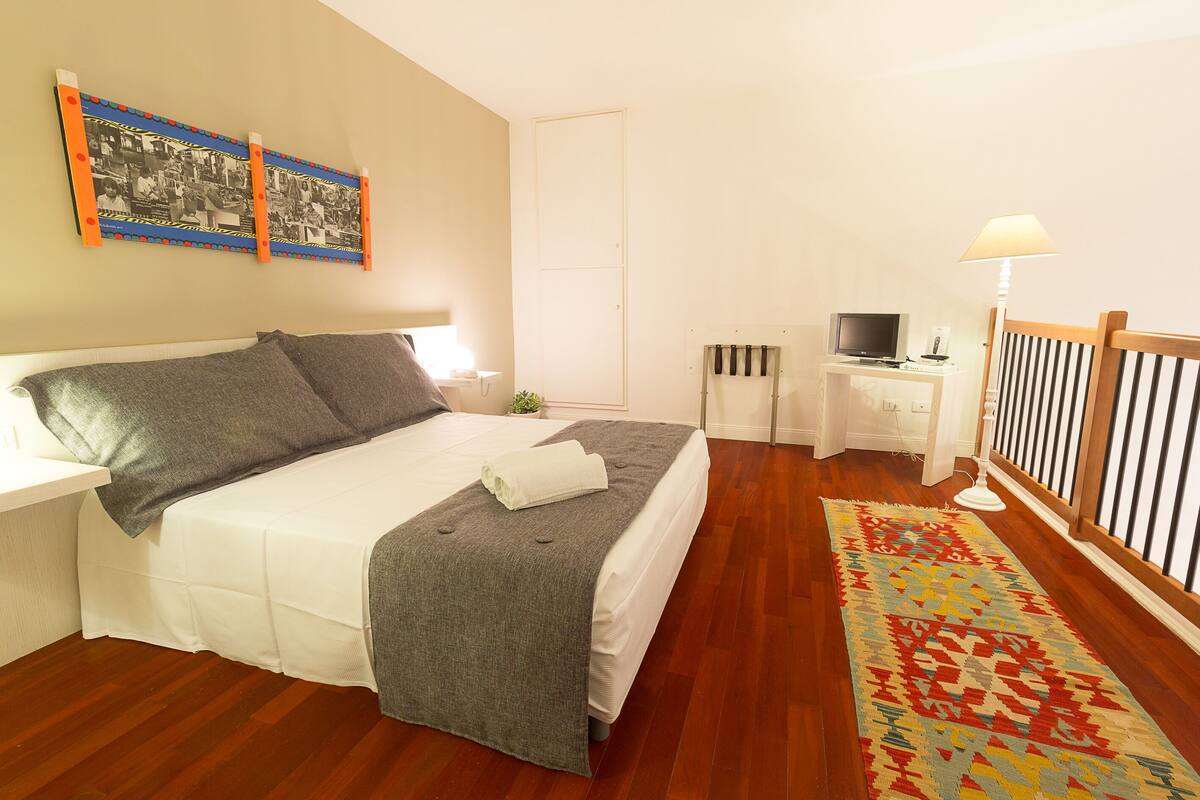 Une chambre à coucher bien rangée, avec un lit, une table de chevet, une télévision et un tapis à motifs.