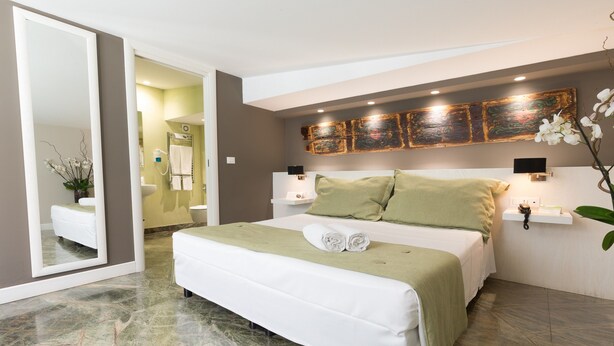 Un dormitorio moderno con una cama grande, una mesita de noche, un espejo y una obra de arte colgada en la pared.