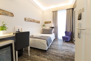 Habitación de hotel con cama, escritorio, silla, mesita, planta en maceta y puerta con número.
