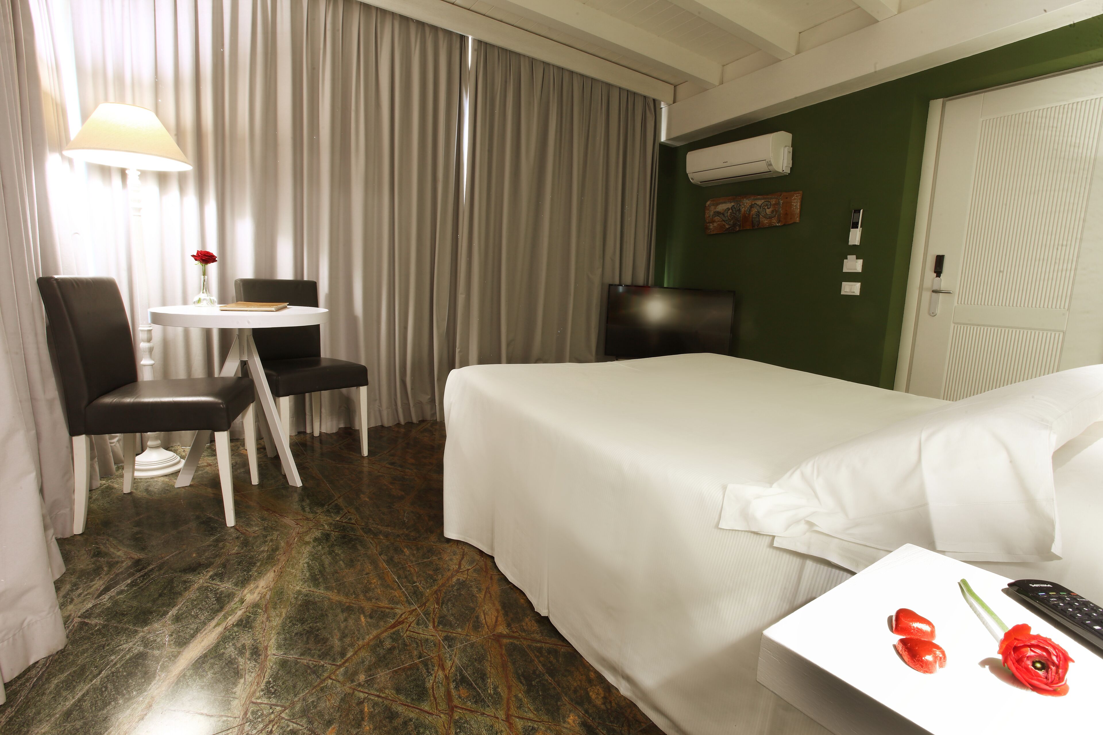 Una camera d'albergo con un letto, una scrivania con una lampada, una sedia e un tavolino con un vaso di fiori.