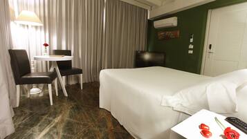 Una camera d'albergo con un letto, una scrivania con una lampada, una sedia e un tavolino con un vaso di fiori.
