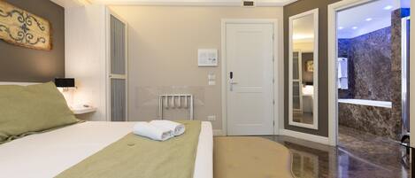 A modern hotel room with a large bed, a bench, a bathroom with a shower, and a view of a rocky landscape.