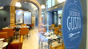 Interior de un restaurante con mesas y sillas, un letrero que dice "Locanda del Gusto" y una pared de ladrillo con arco.