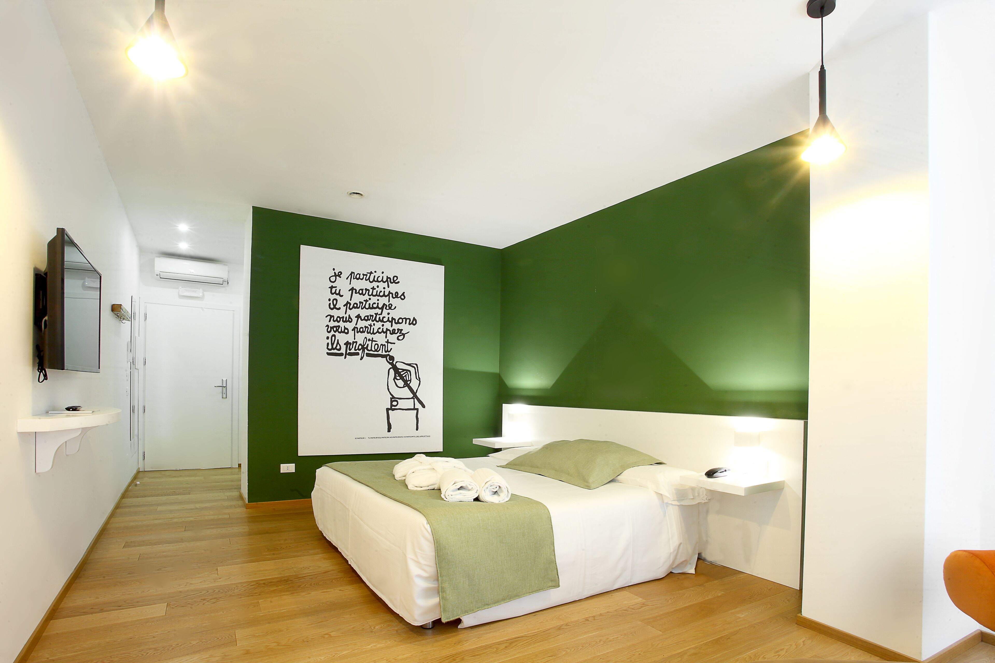 A modern bedroom with a green accent wall, a white bed, a bedside table with a lamp, and a poster on the wall.