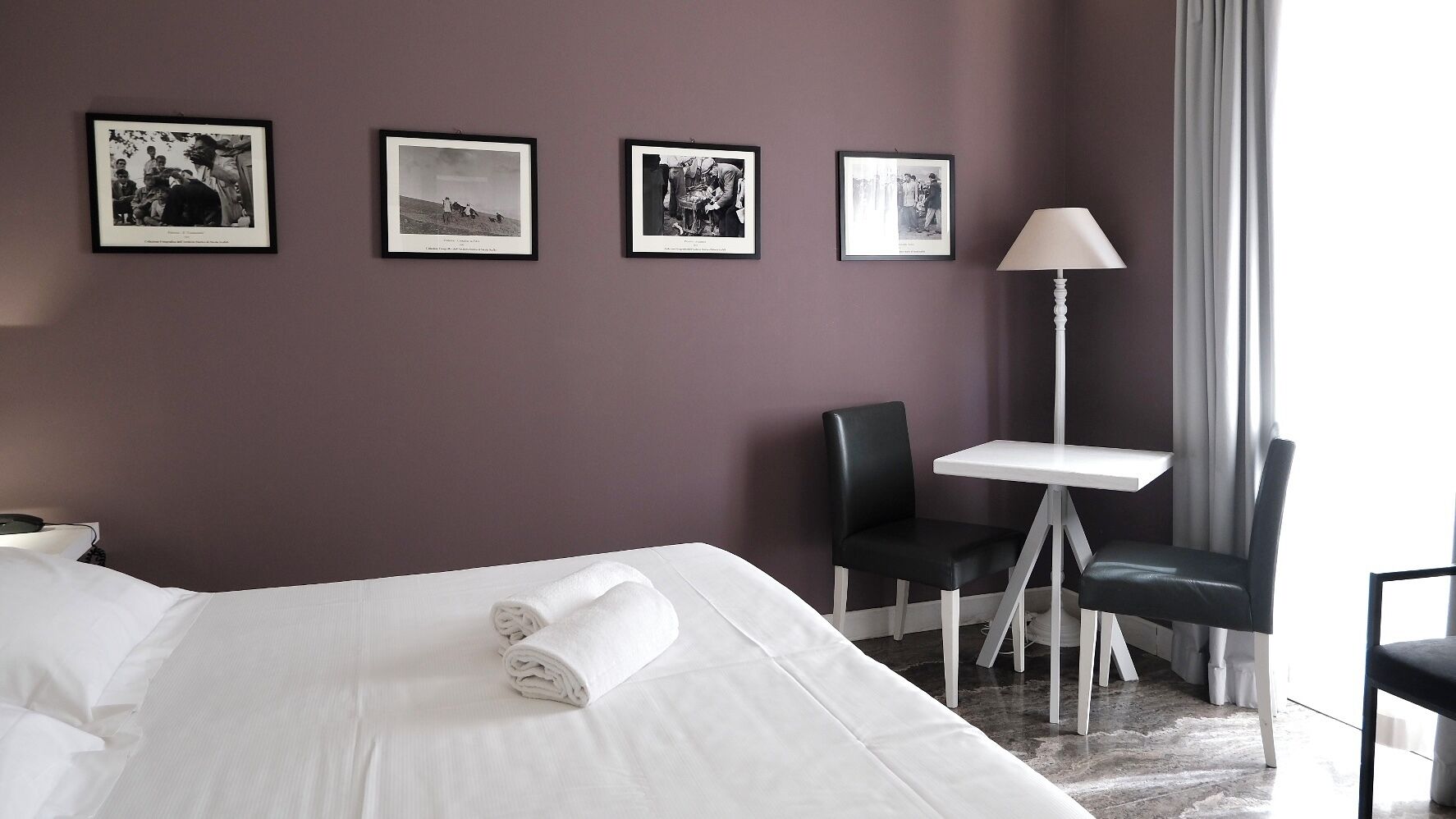 Ein Hotelzimmer mit einem Bett, zwei Stühlen, einem kleinen Tisch und drei gerahmten Bildern an der Wand.