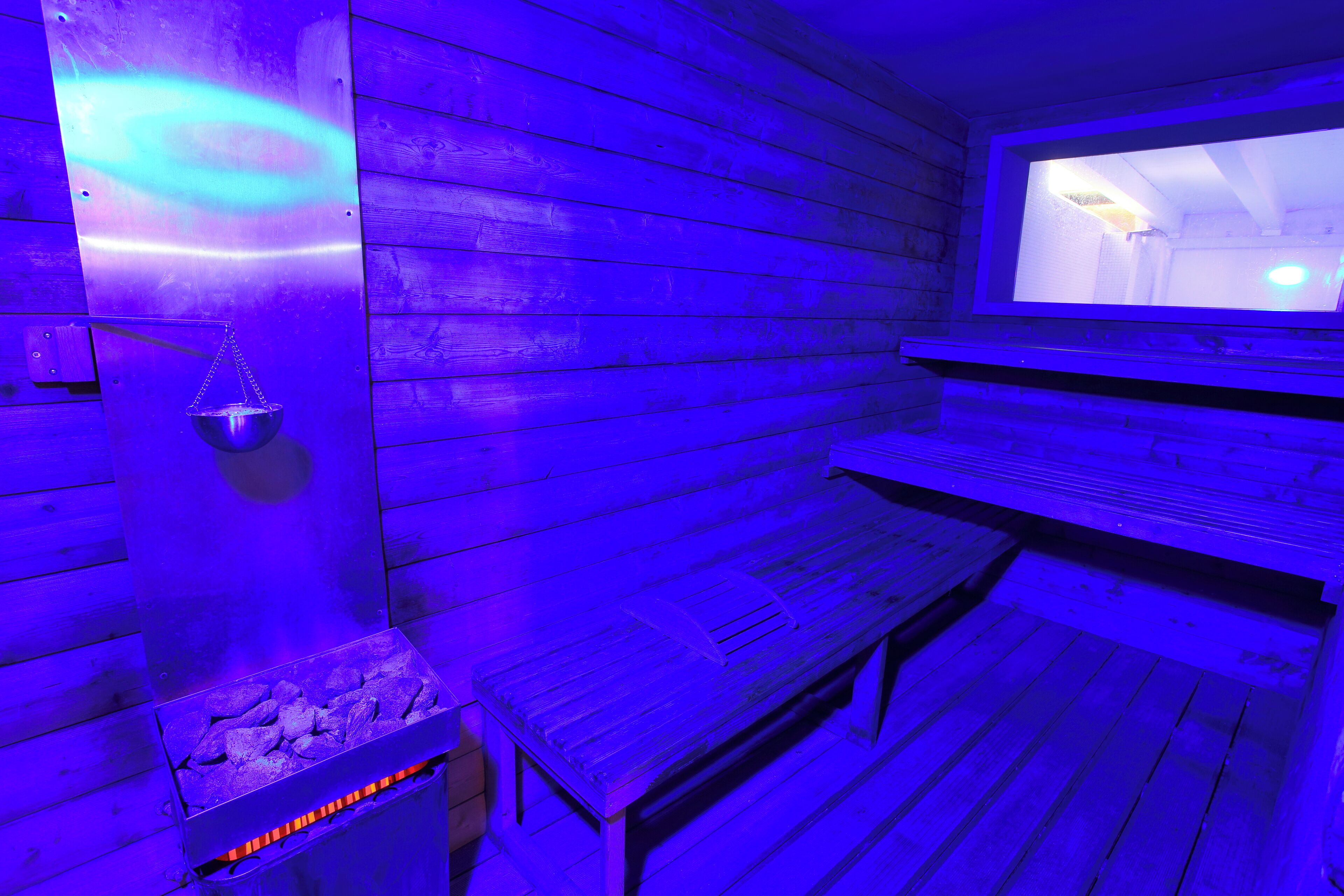 Un sauna avec des murs en bois, un banc et un bassin en pierre.