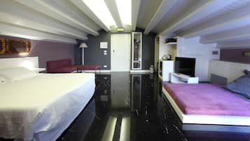 A modern hotel room with a large bed, a smaller bed, a TV, and a seating area.