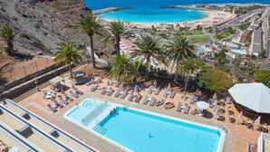 A resort with a swimming pool, palm trees, and a view of the ocean. - Hotel Chatur Palmera Mar (Mogan)