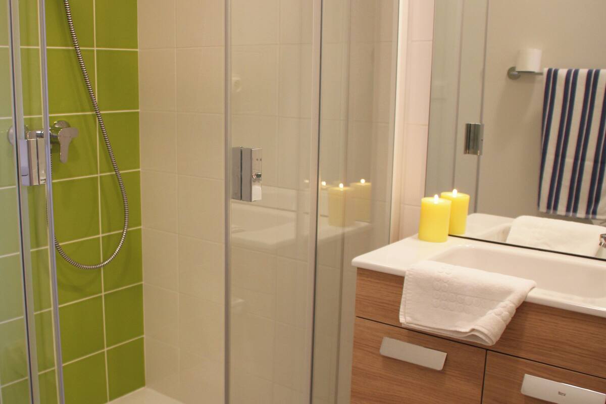 Une salle de bain moderne avec une douche à parois de verre, un meuble-lavabo en bois avec un miroir et deux bougies allumées posées sur le plan de travail.