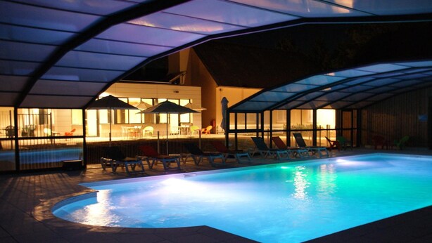 A swimming pool with lounge chairs and umbrellas under a covered area.