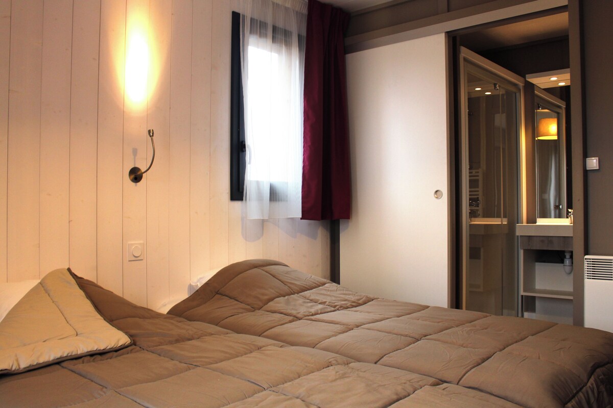 Een slaapkamer met een bed, een raam met dunne gordijnen en een deur naar een badkamer.