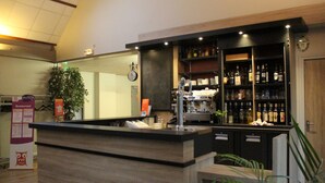 A bar area with a wooden counter, shelves with bottles, a clock, and a potted plant.