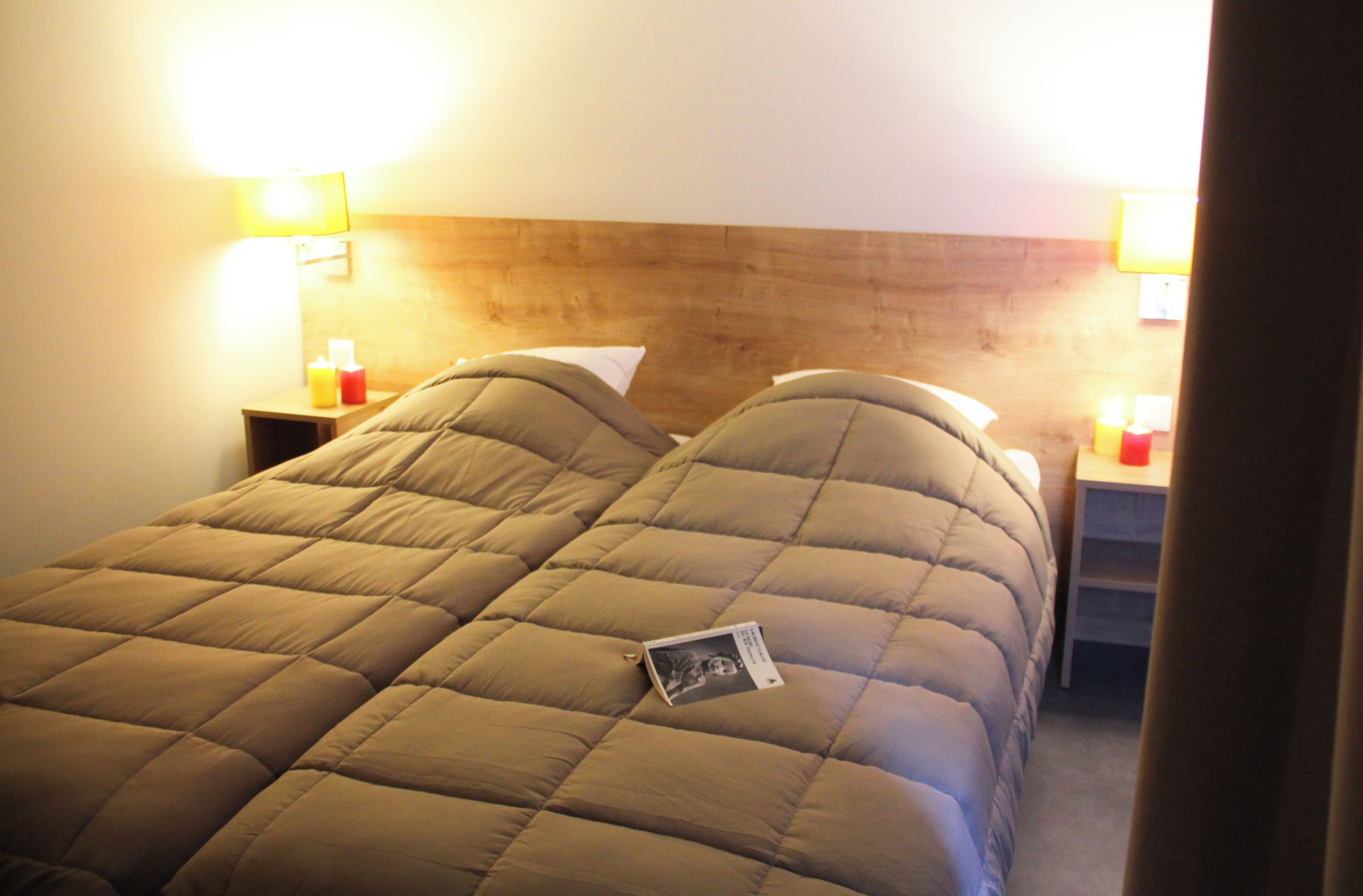 Een bed met hoofdeinde, twee nachtkastjes met lampen, en een bijzetmeubel met een fles.