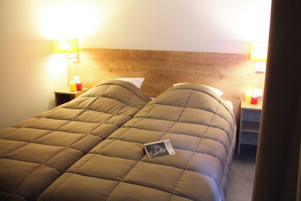 Un lit avec une tête de lit, deux tables de chevet avec des lampes et une petite table de nuit avec une bouteille.