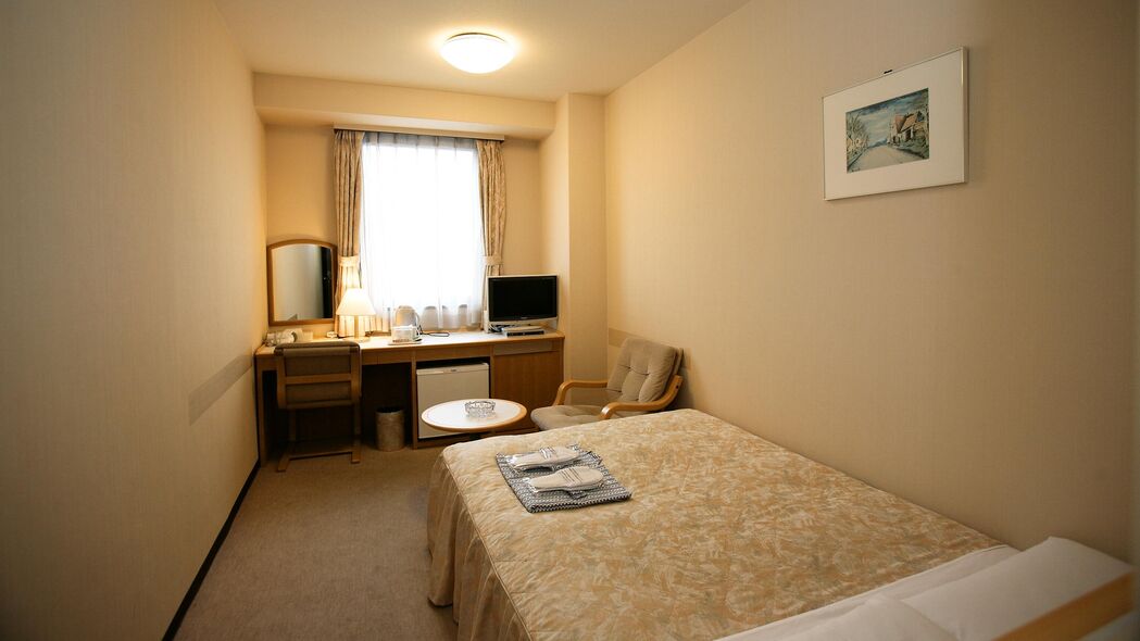 A hotel room with a bed, a desk with a computer, a chair, and a small table.