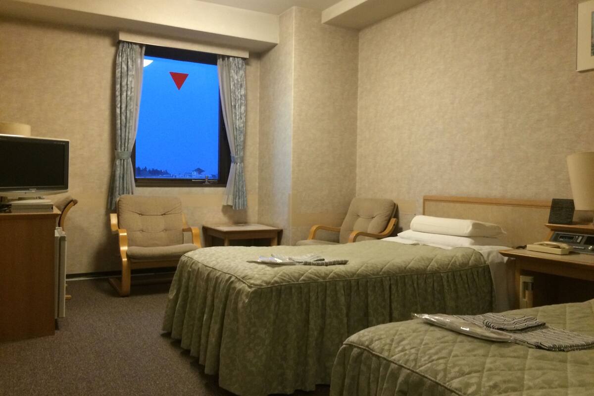 A hotel room with two beds, a TV, a desk with a lamp, and a window with curtains.