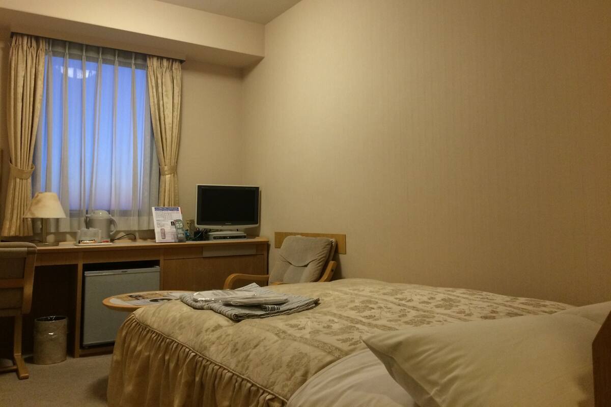 A hotel room with a bed, a desk with a computer, a lamp, and a window with curtains.