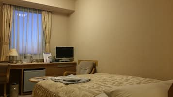 A hotel room with a bed, a desk with a computer, a lamp, and a window with curtains.
