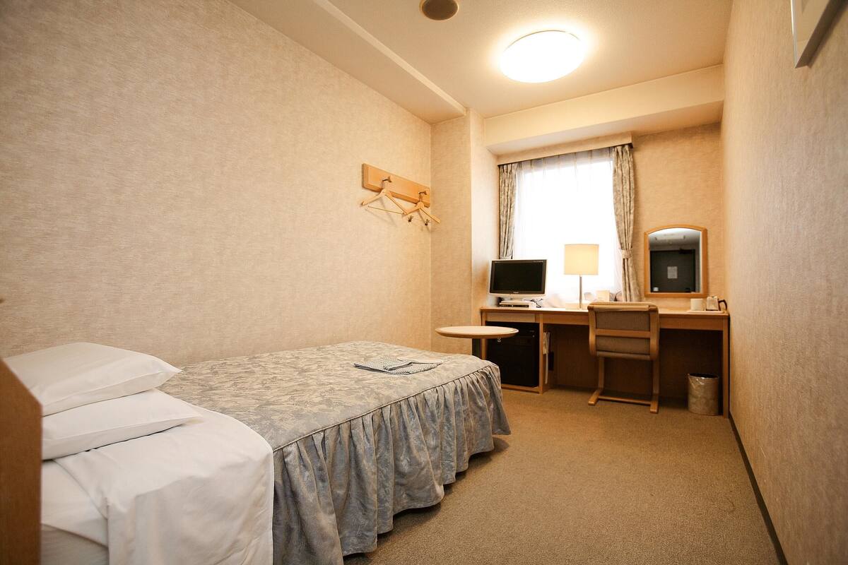 A hotel room with a bed, desk, chair, TV, lamp, and a mirror.