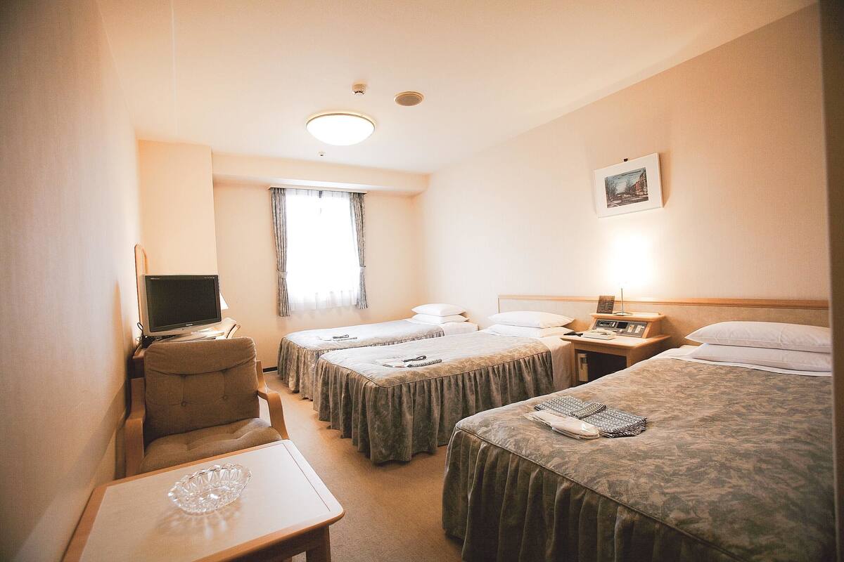 A hotel room with three beds, a desk, a television, and a window with curtains.