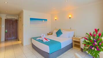 Een hotelkamer met een bed, een nachtkastje, een aan de muur bevestigd telefoon, een schilderij van een strand en een bloemstuk.