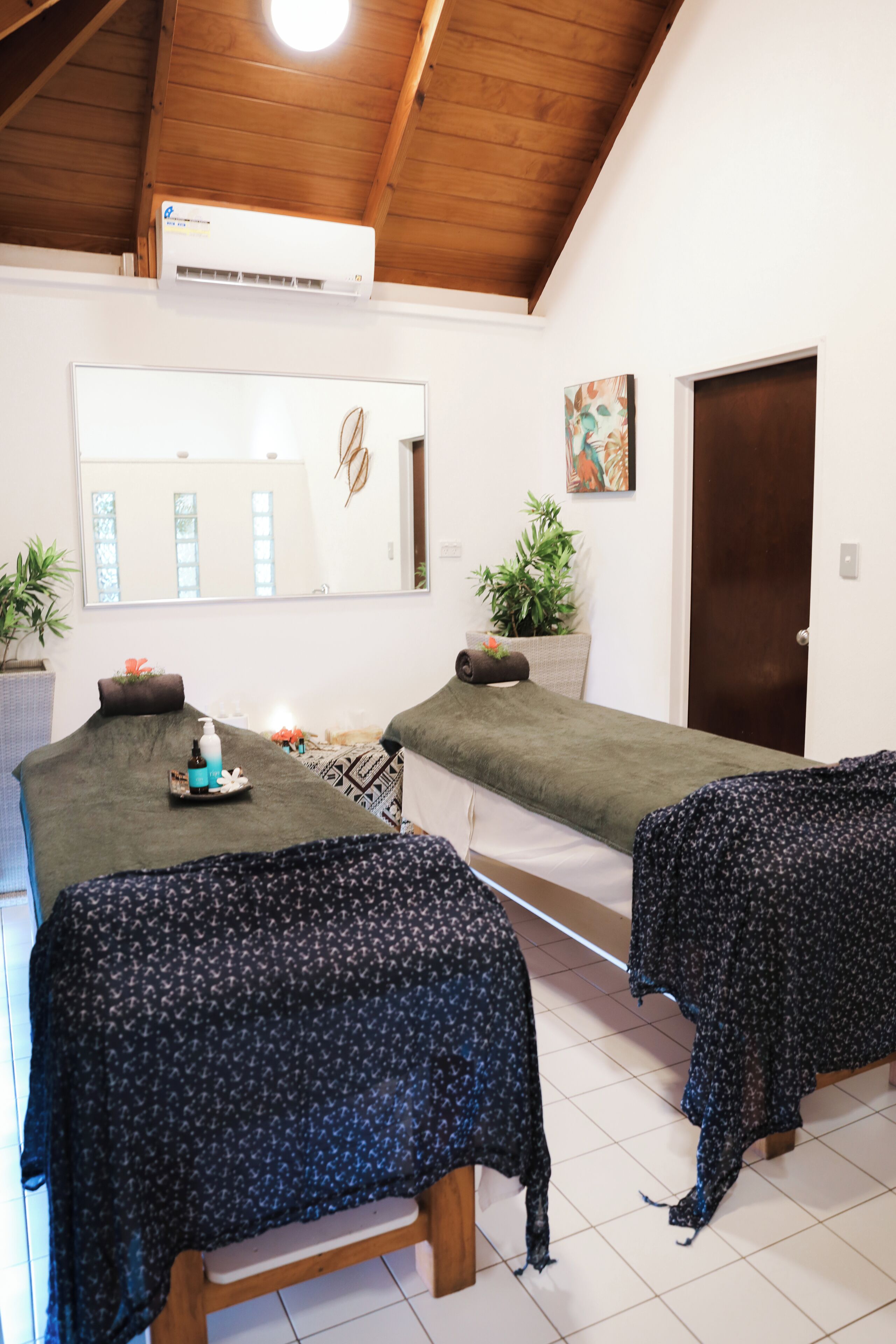 A room with two massage tables, a mirror, a door, and a potted plant.