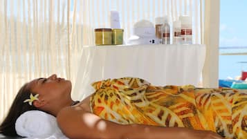 A person lying on a massage table with a towel and a flower in their hair, surrounded by various spa products on a table.