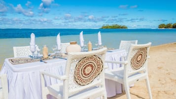 Un montaje para comer frente al mar con sillas de mimbre blanco y una mesa dispuesta para dos.