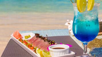 Una bandeja de mariscos con una bebida sobre una mesa junto a la playa.