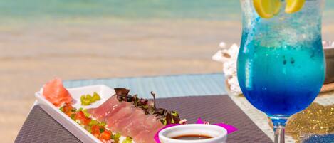 A seafood platter with a drink on a table by the beach.