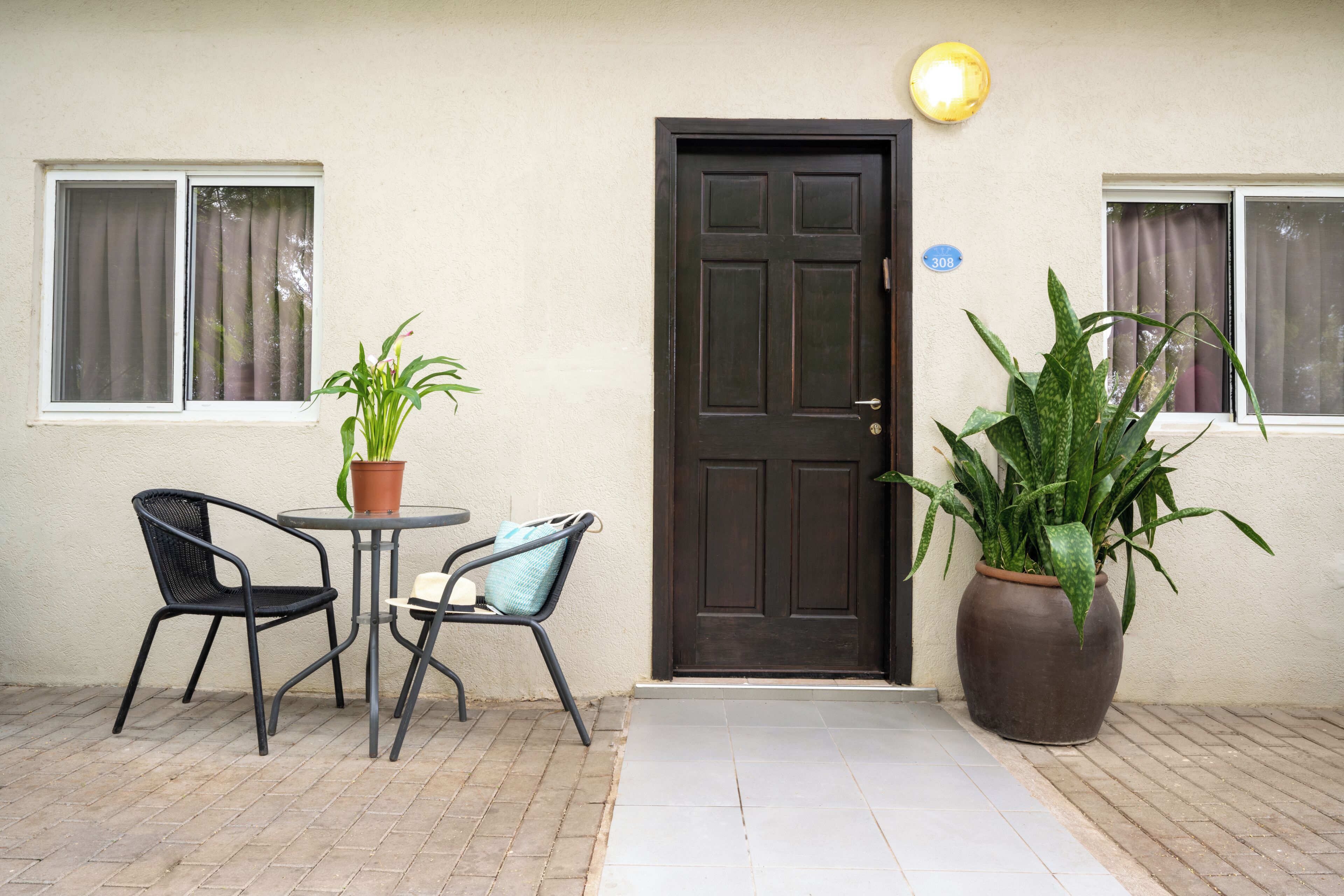 Une porte avec une plaque portant un numéro, un pot de fleurs et deux chaises devant un bâtiment.