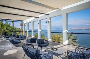 Un patio exterior con mobiliario de mimbre, una mesa con una botella y vasos, y vista al mar.