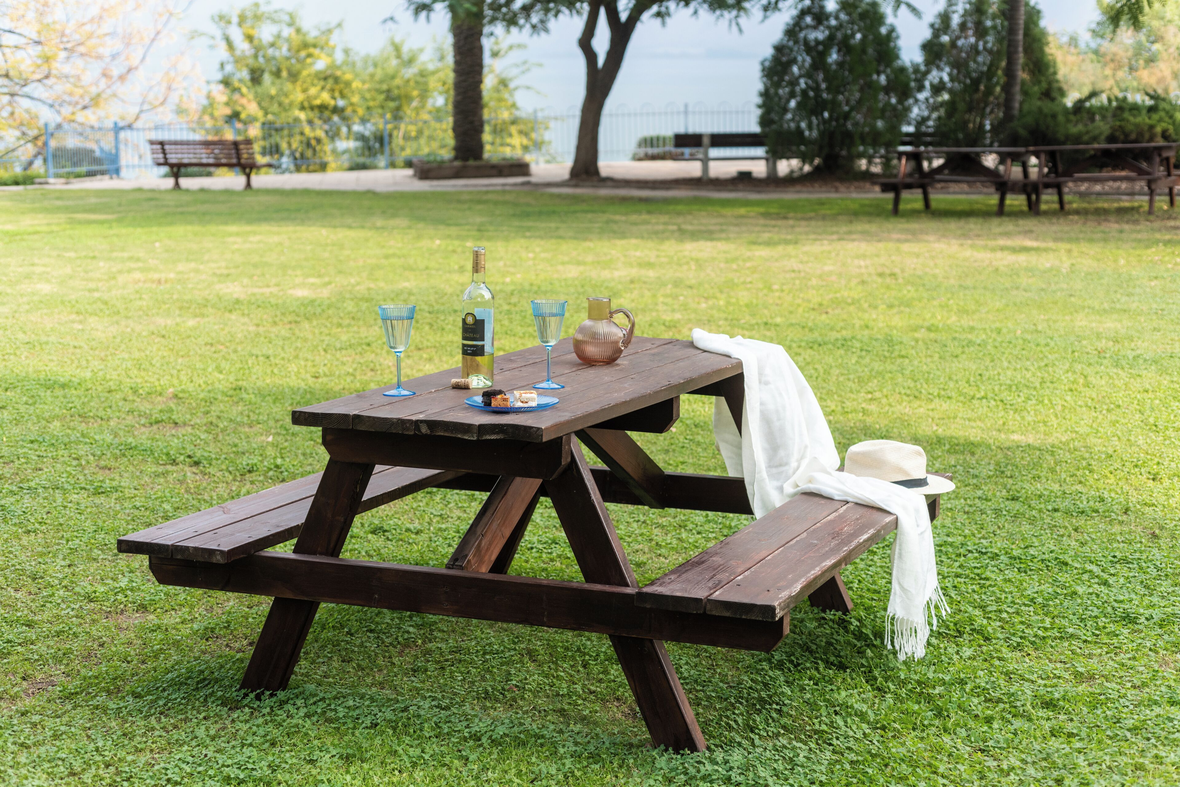 A picnic table with a bottle, glasses, and a pitcher on it.