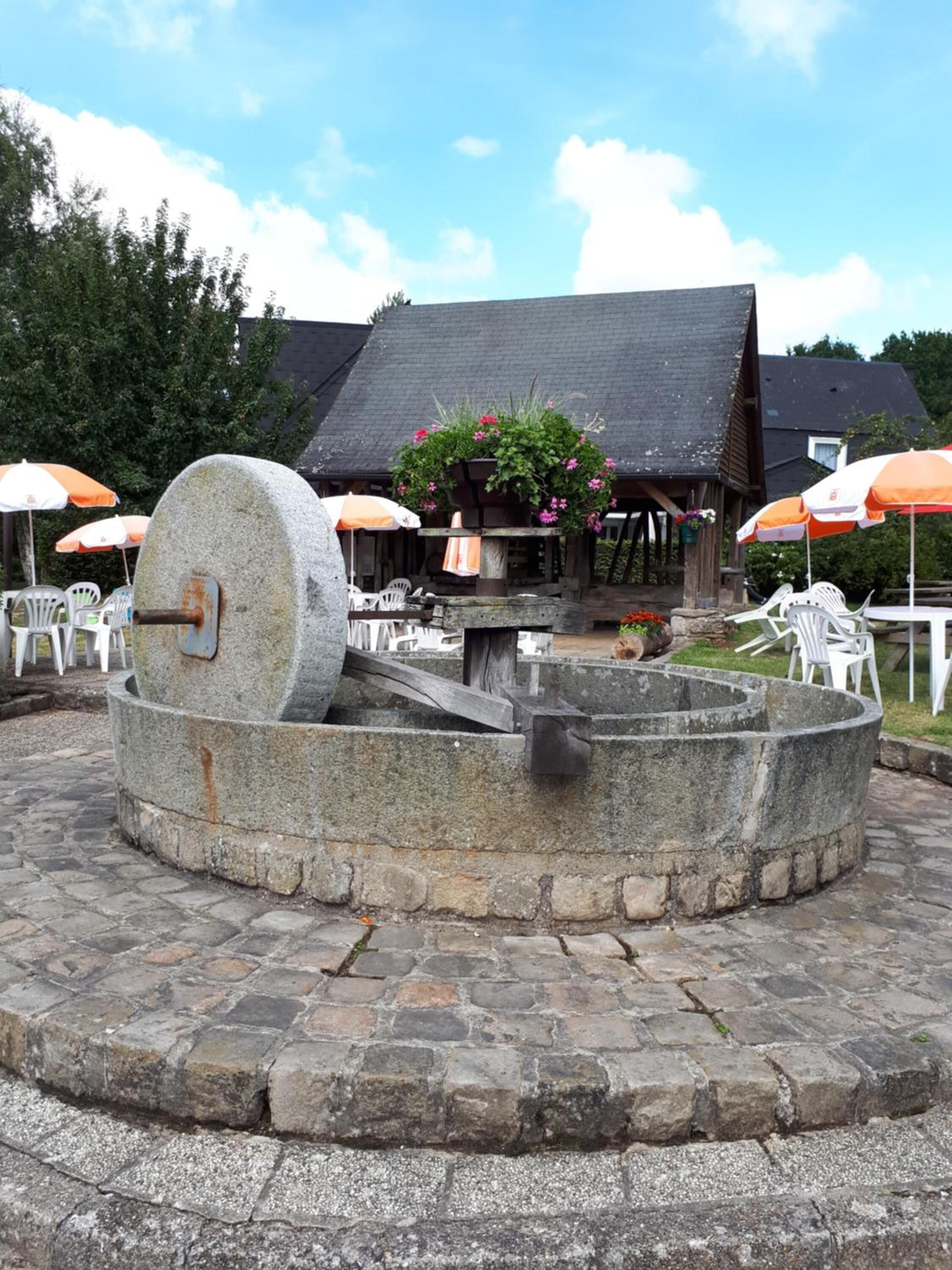 A stone well with a crank handle, surrounded by stone steps and outdoor seating with umbrellas.
