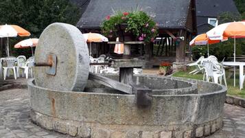 A stone well with a crank handle, surrounded by stone steps and outdoor seating with umbrellas.