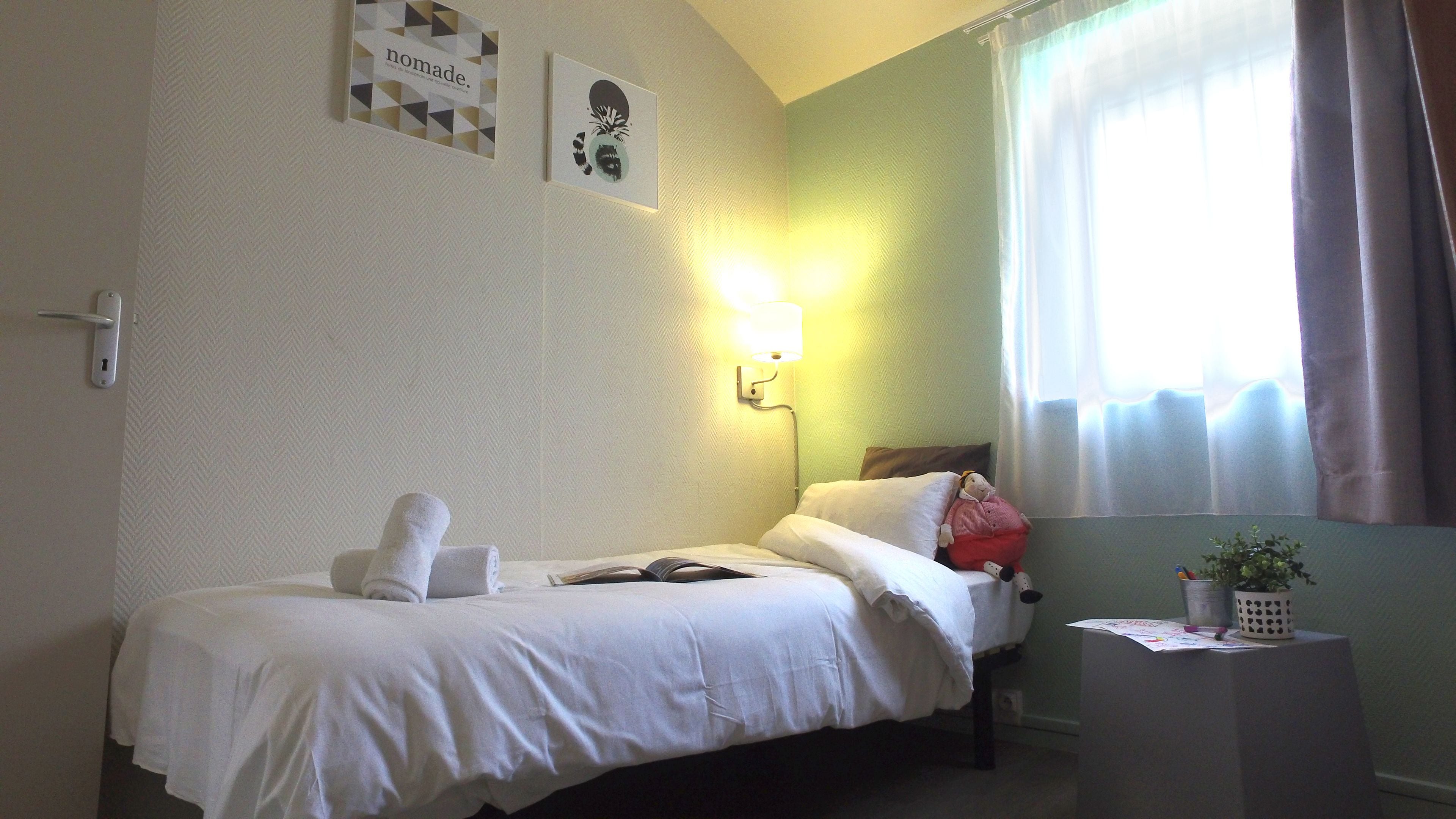 A hotel room with a bed, a nightstand, a lamp, a window with curtains, and wall decorations.