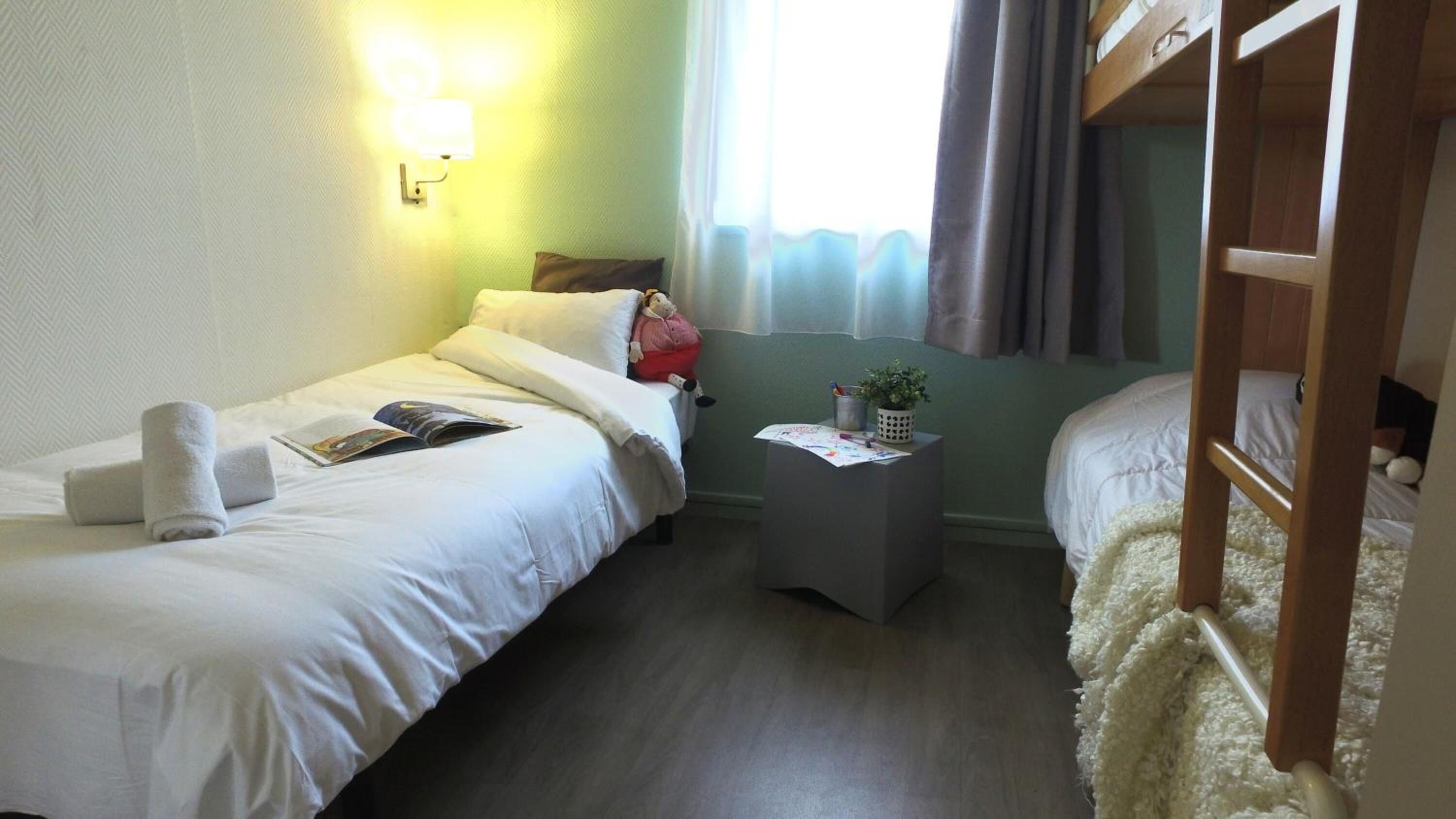 A hotel room with two beds, a small bedside table with a plant, and a wall-mounted light fixture.