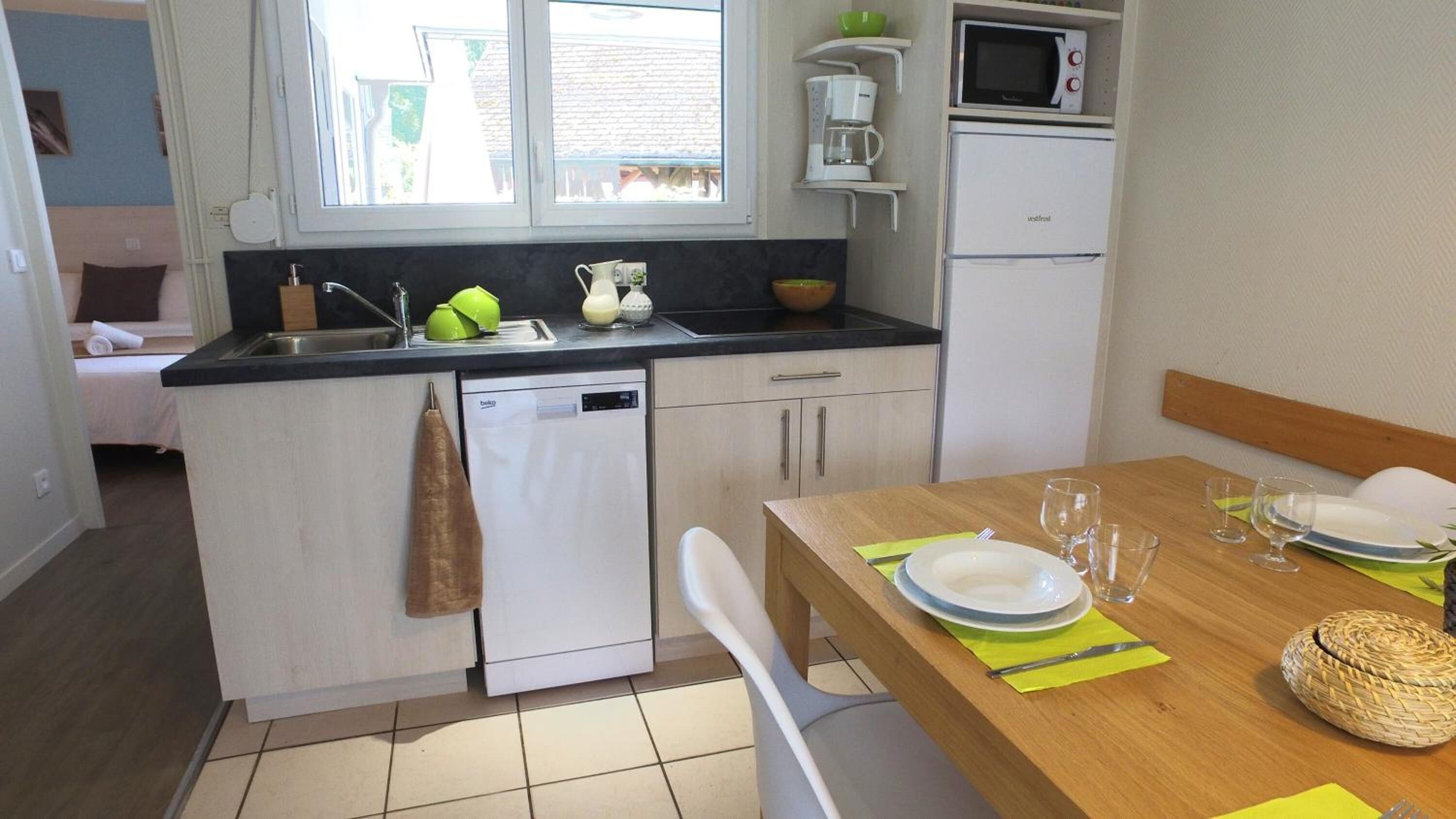 Una cocina compacta equipada con lavavajillas, microondas y cafetera. Hay una mesa de comedor con platos y vasos preparados para dos personas.